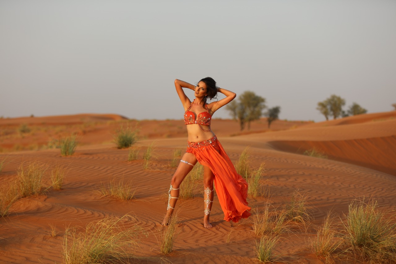 Lizzie in a coral costume dancing on desert dunes